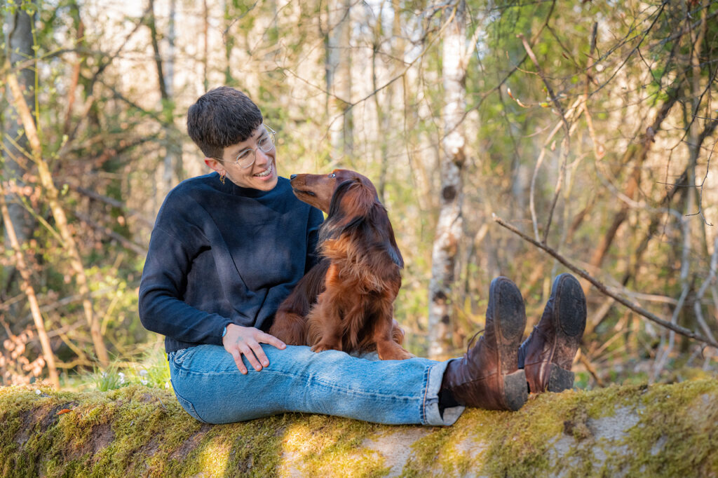 Dackel und Frau auf moosbewachsenem Baumstamm