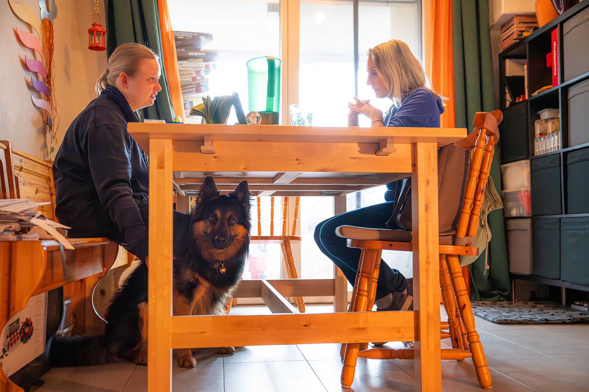 Zwei Personen sitzen mit Assistenzhund am Tisch