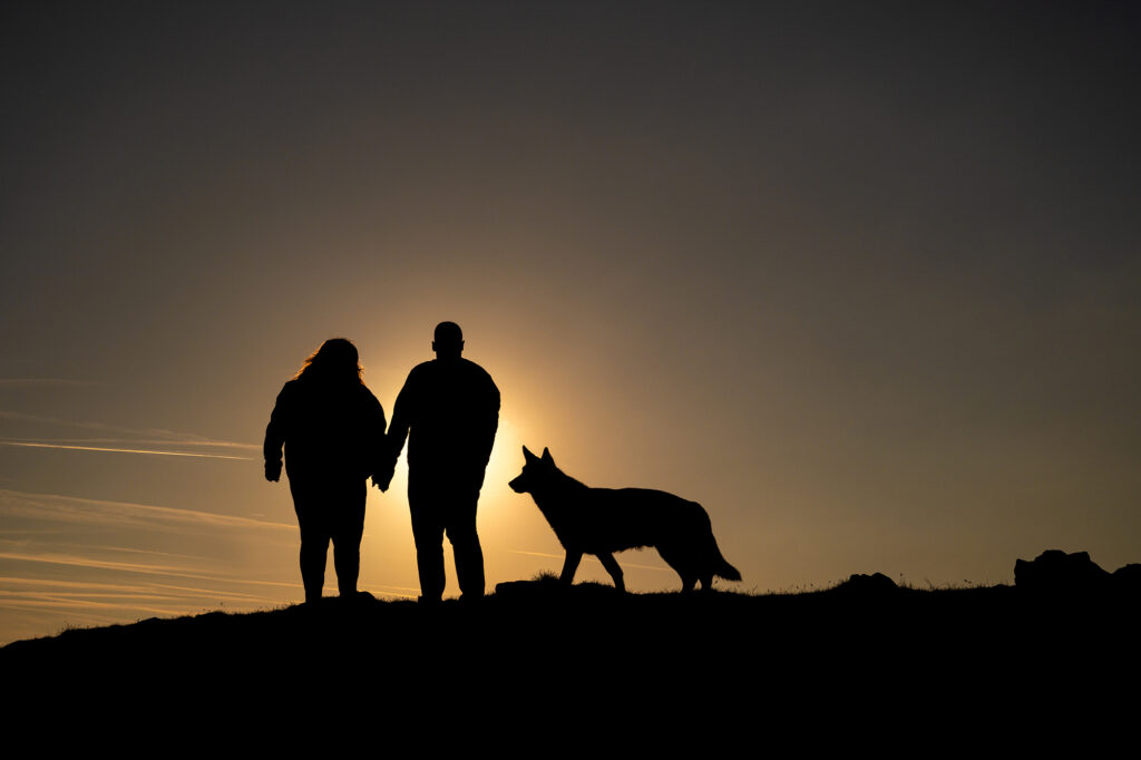 Paar steht mit Hund im Sonnenuntergang