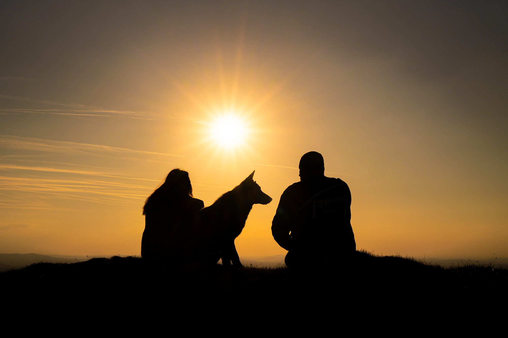 Paar sitzt mit Hund im Sonnenuntergang