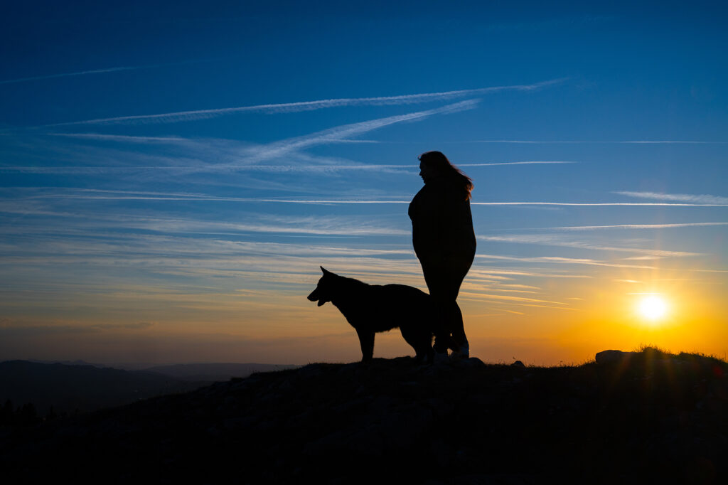Frau steht mit Hund im Sonnenuntergang