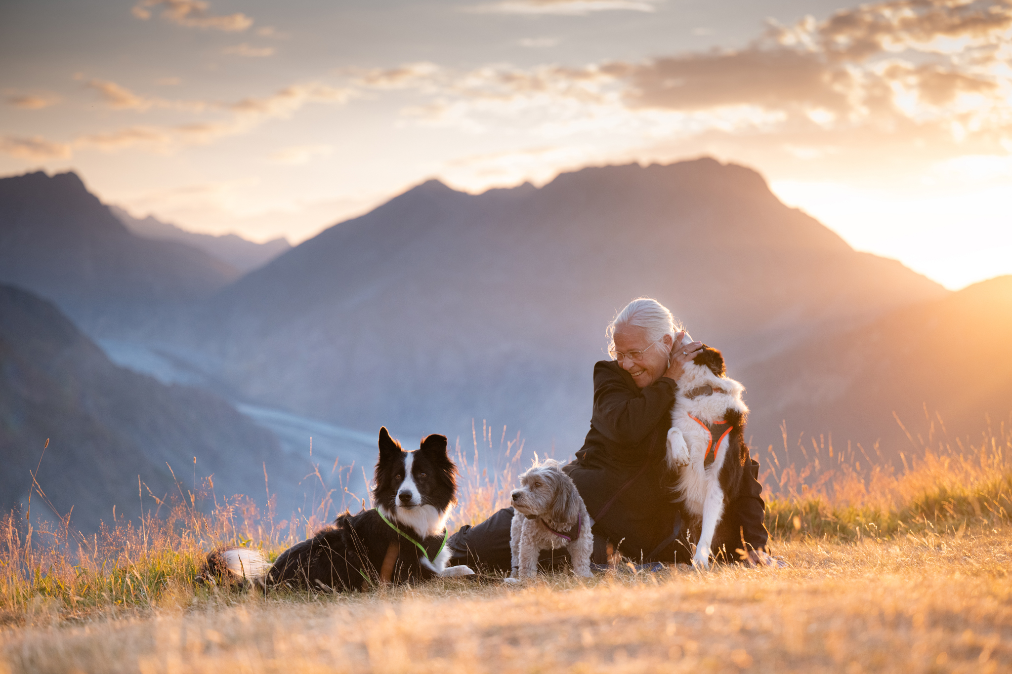 Frau mit drei Hunden beim Sonnenaufgang